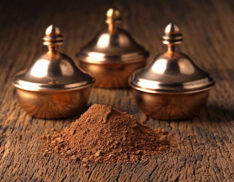 Bronzeankauf Drei Kupferbehälter neben einem Häufchen Kakaopulver auf einer Holzoberfläche.