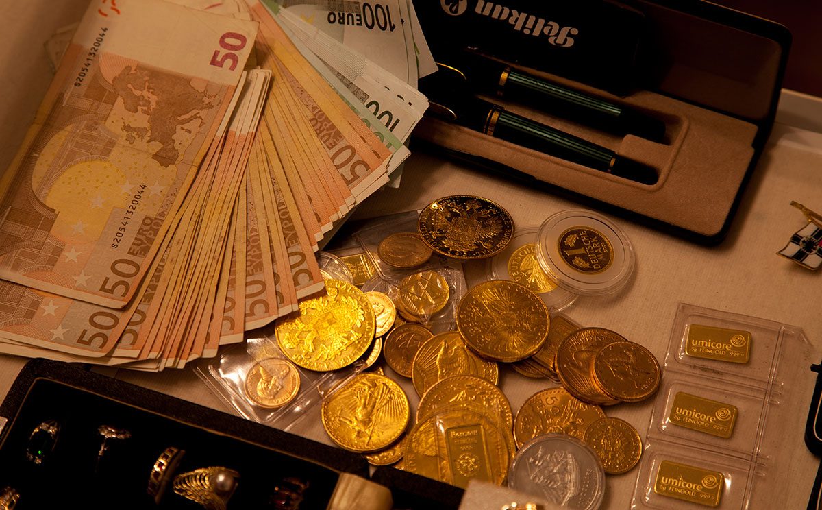 Goldankauf Ein Haufen Geldscheine, Münzen und Goldbarren auf einem Tisch.